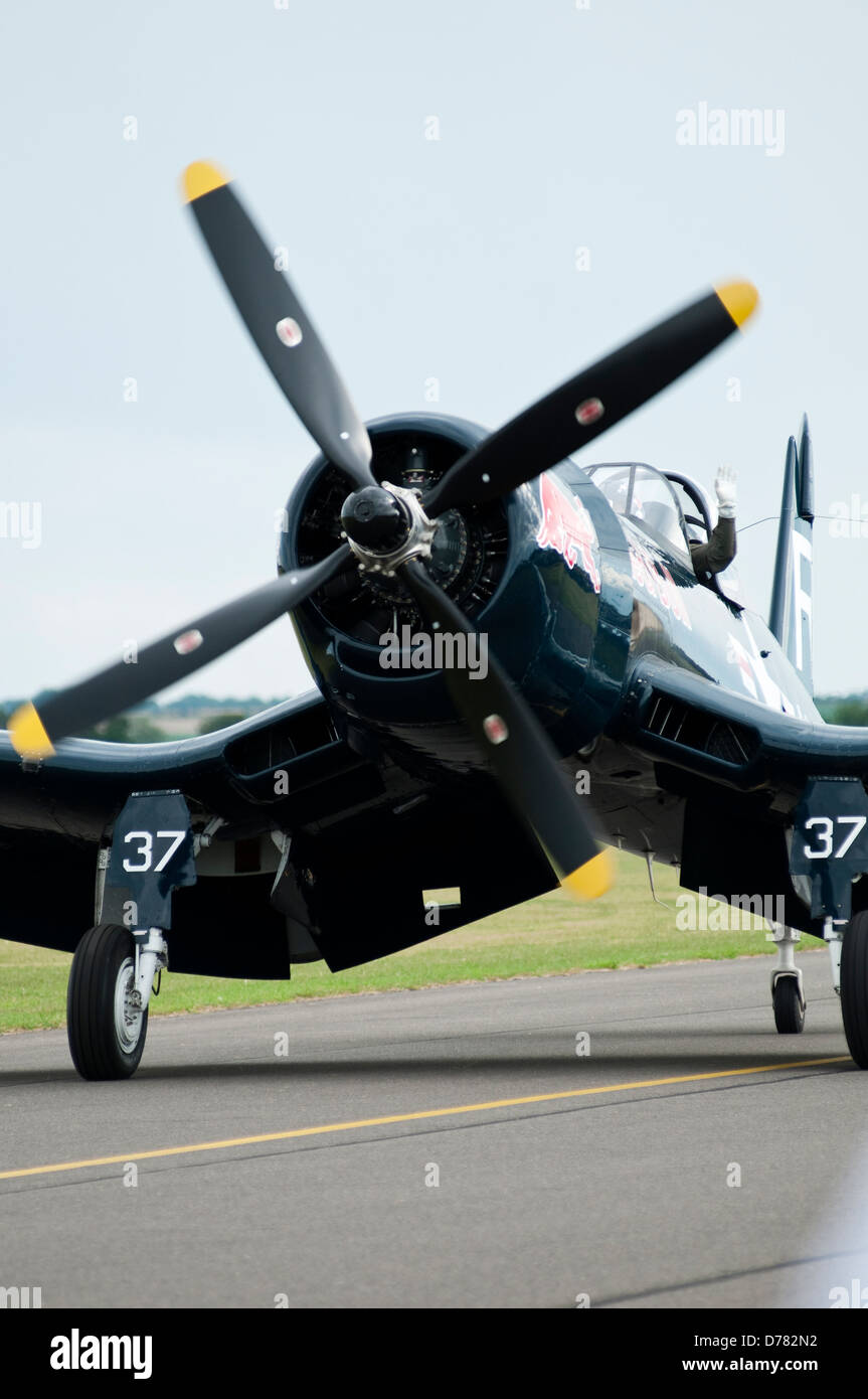 A vintage US Navy 'Corsair' fighter plane is seen taxing along an airfield runway, the pilot waving from an open cockpit. Stock Photo