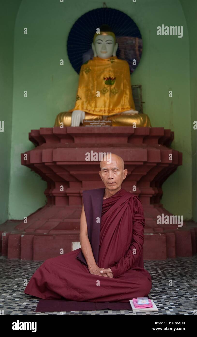 Ein buddhistischer Mönch sitzt am 30.03.2013 an der Shwedagon-Pagode in Rangun, Myanmar, vor einer Buddha Figur. Foto: Sebastian Kahnert Stock Photo