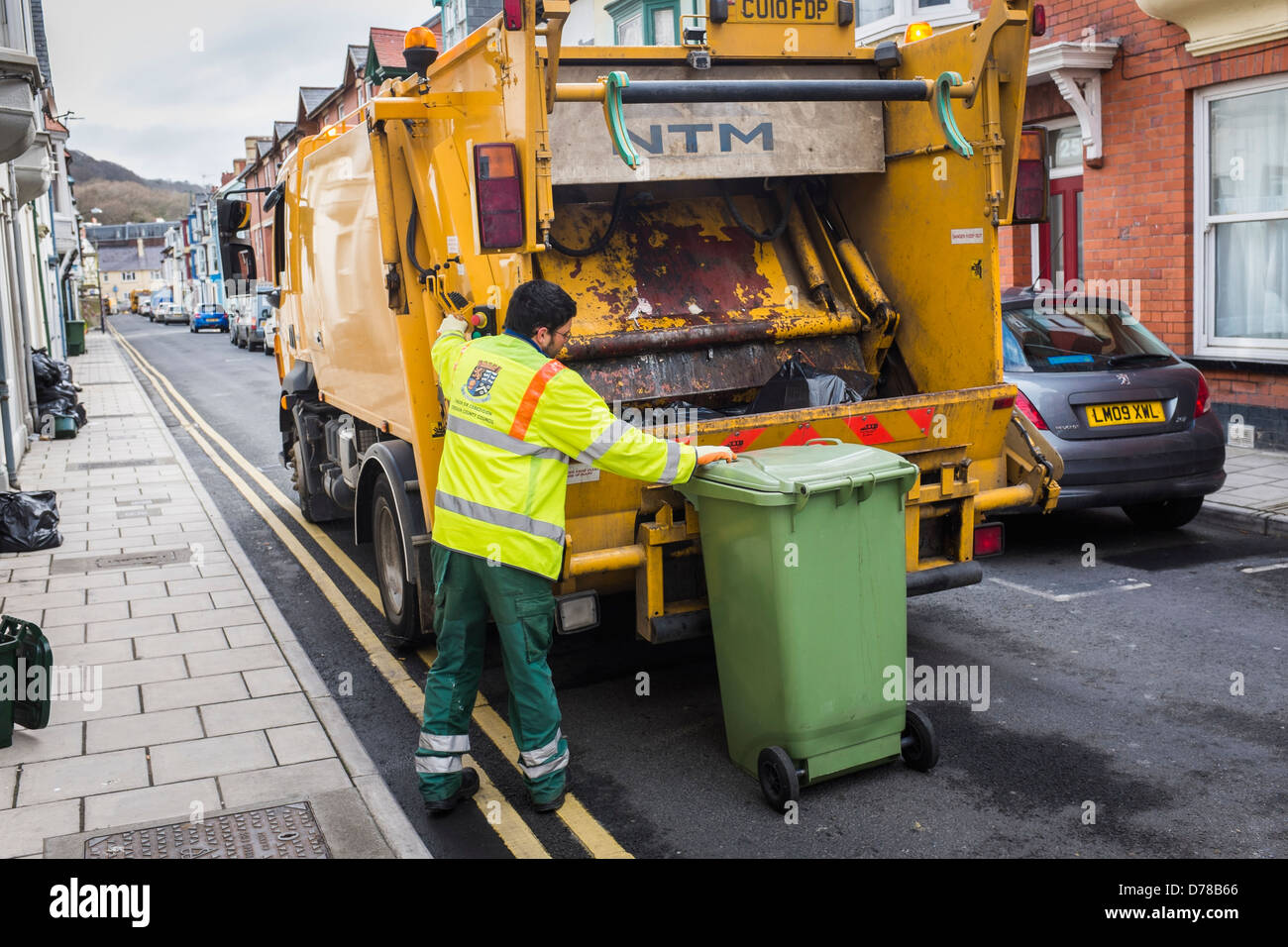Local authority rubbish collection day green wheelie bin being loaded