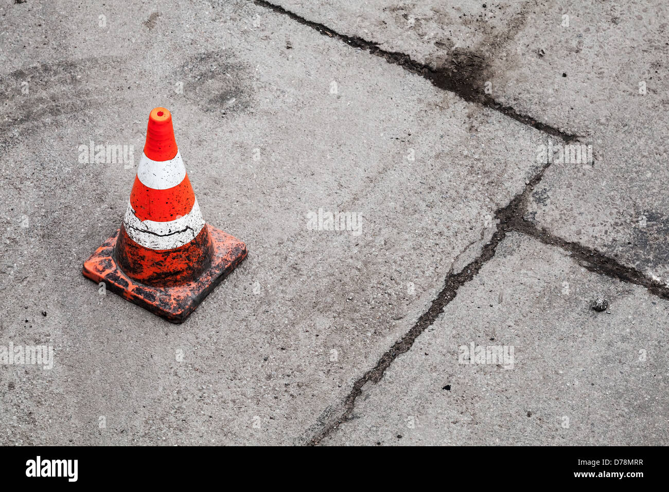 Red and white striped warning cone on dirty asphalt road Stock Photo