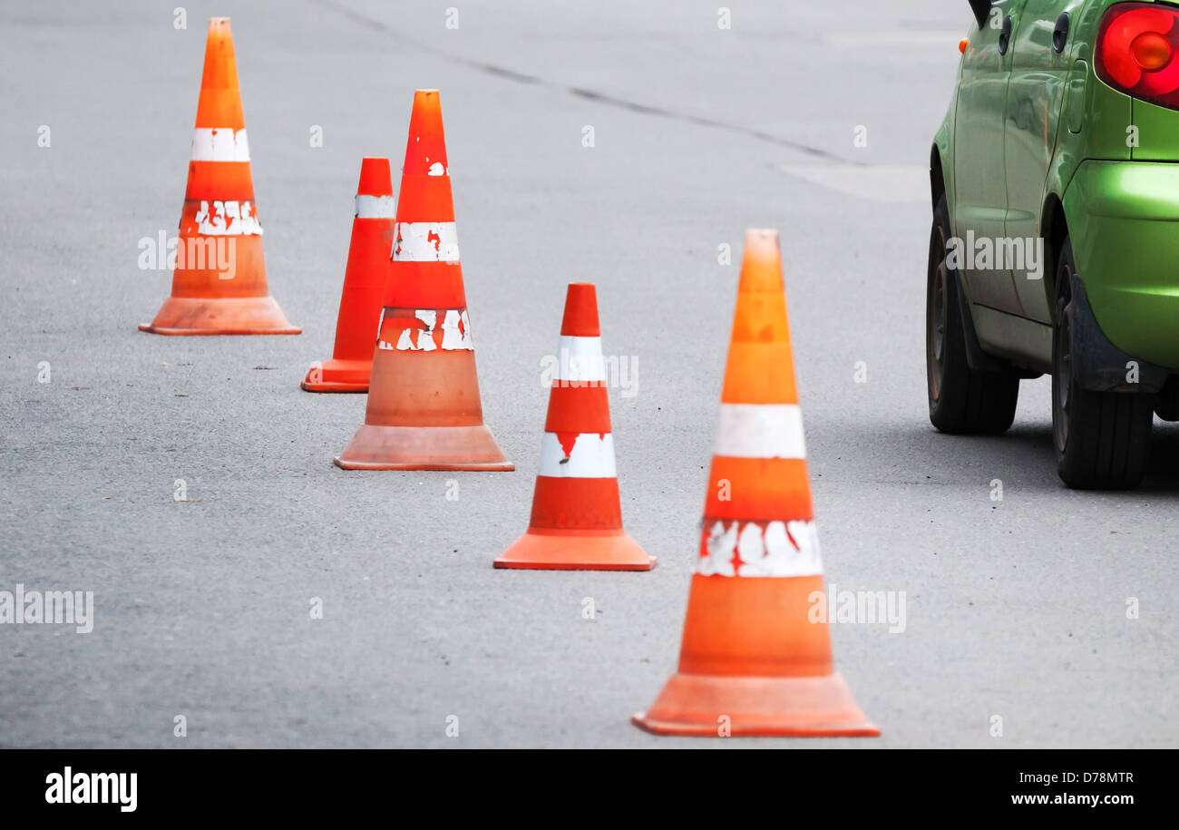Striped orange cones and car fragment on the asphalt road Stock Photo