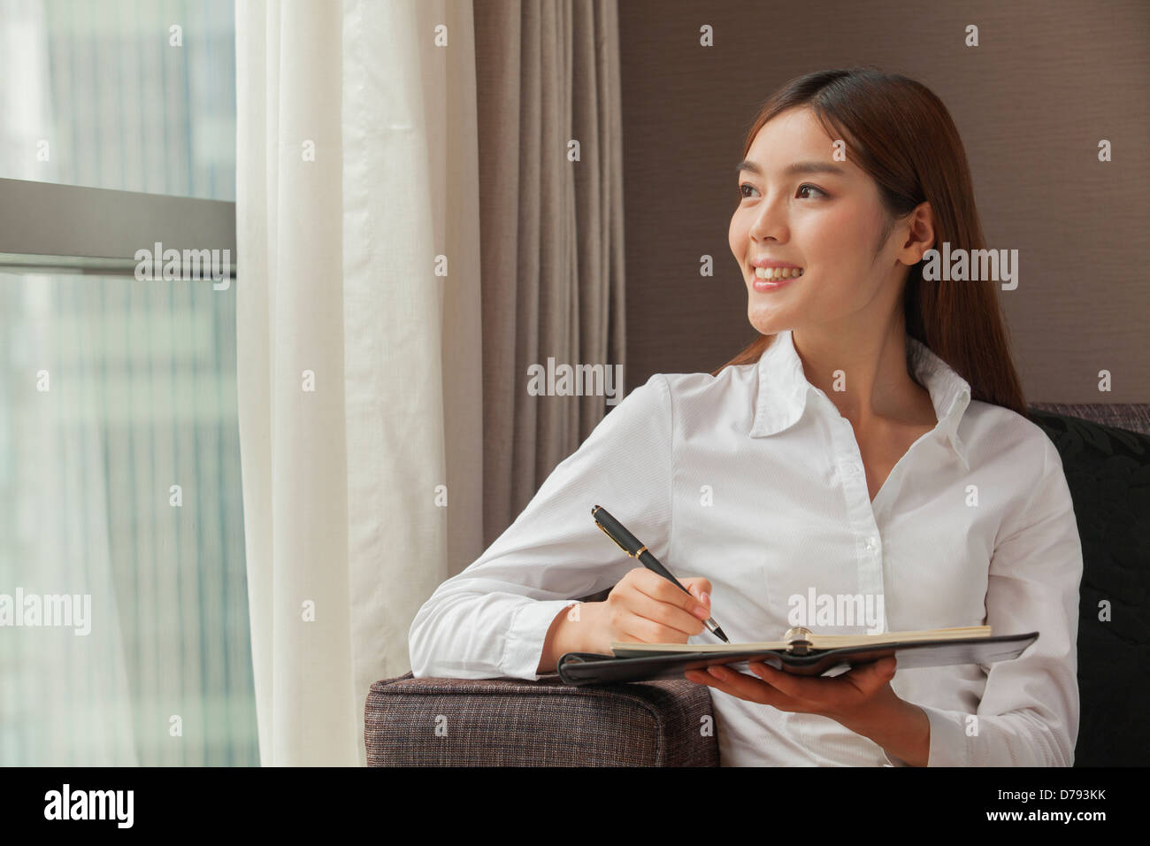 Businesswoman taking notes and looking at the window Stock Photo