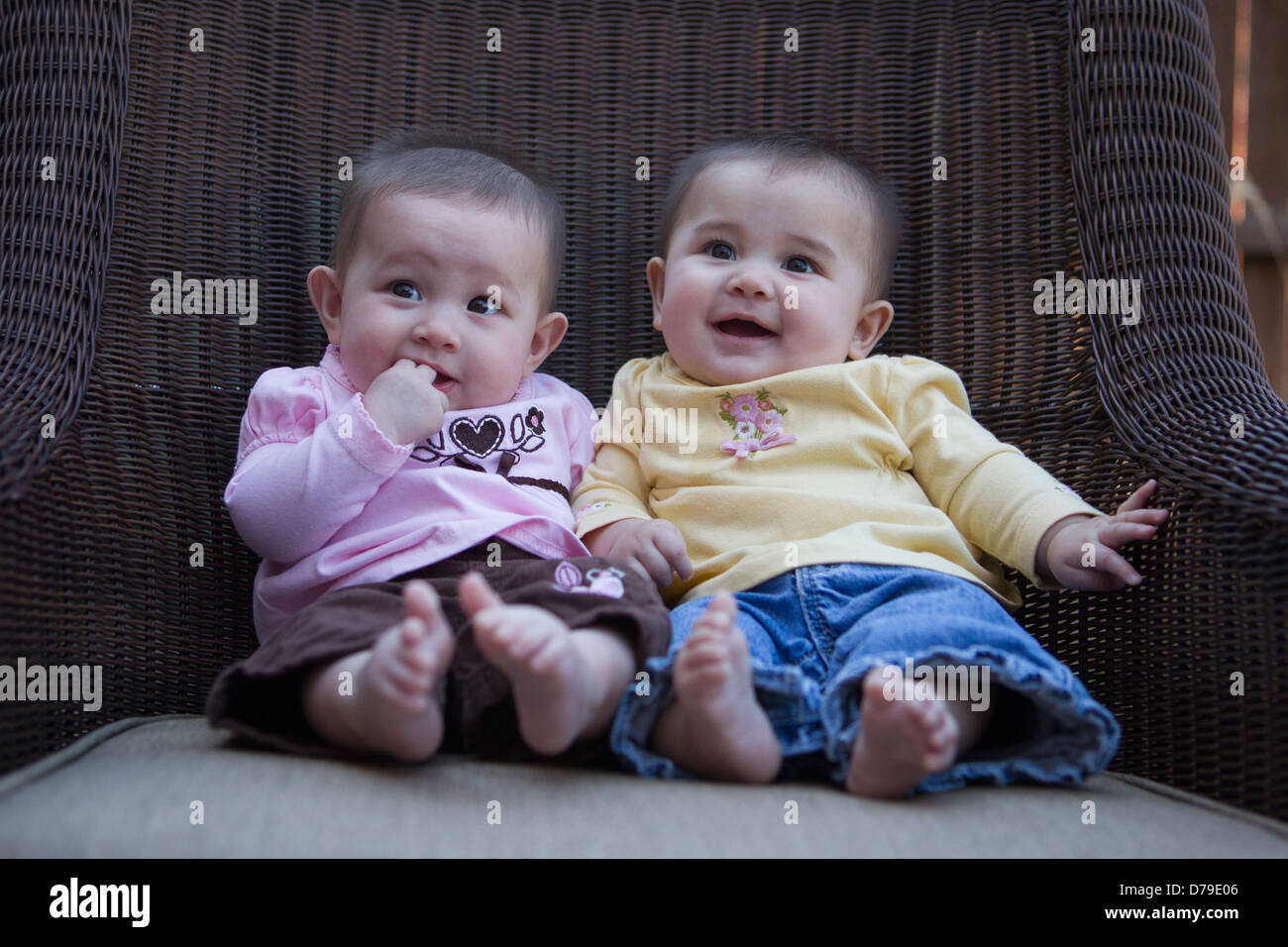 Co-regents, five-month-old twin girls, hold court from their wicker throne. They are happy now as the household is obeying them. Stock Photo