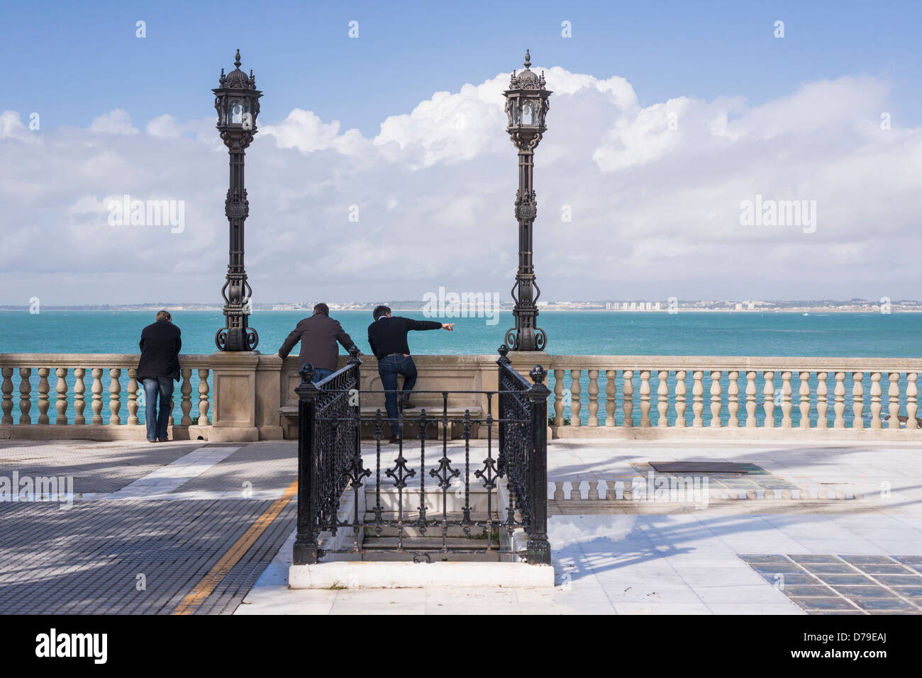 Three men looking out to sea on seafront promenade Cadiz Andalusia Spain Stock Photo