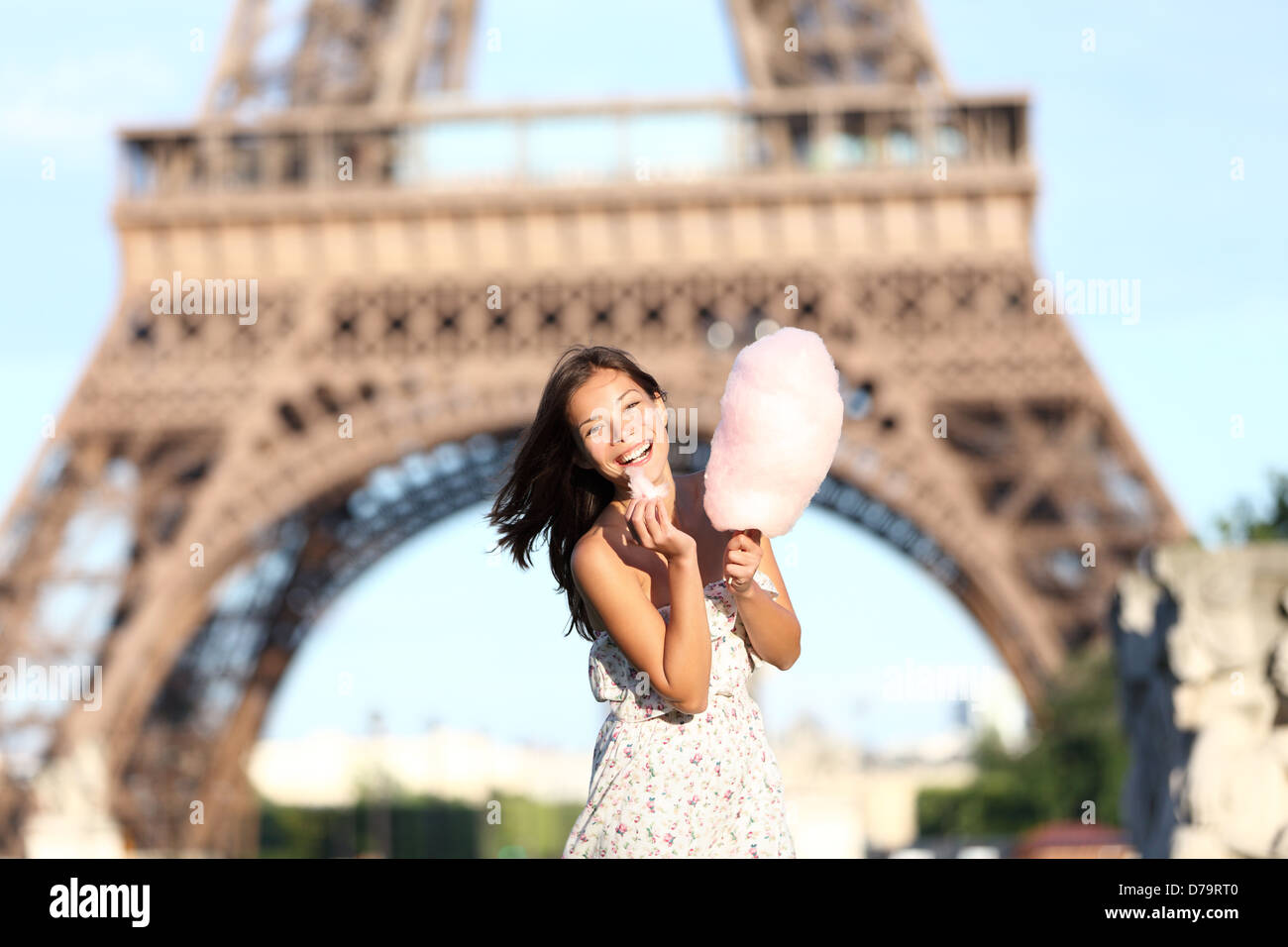 Paris Eiffel Tower woman smiling happy and cheerful eating cotton candy in front of Eiffel Tower in Paris, France. Cute Asian / Caucasian girl. Stock Photo