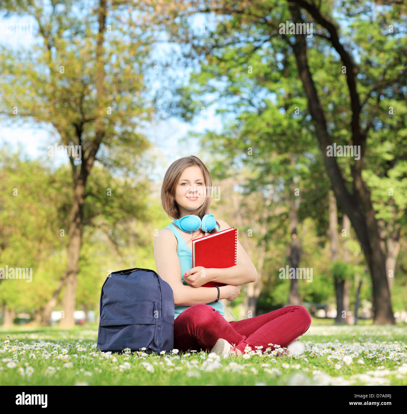 A beautiful young female student with book and headphones sitting on a grass in a park Stock Photo