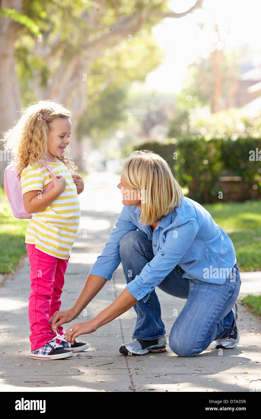 Mother Helping Daughter Tie Shoe Laces On Walk To School Stock Photo