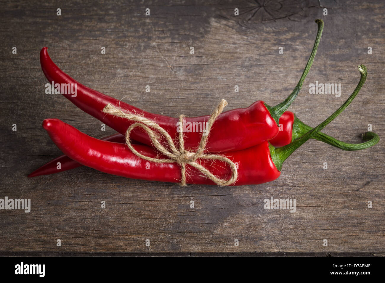 tied red chili peppers on old wooden table, with scratches Stock Photo