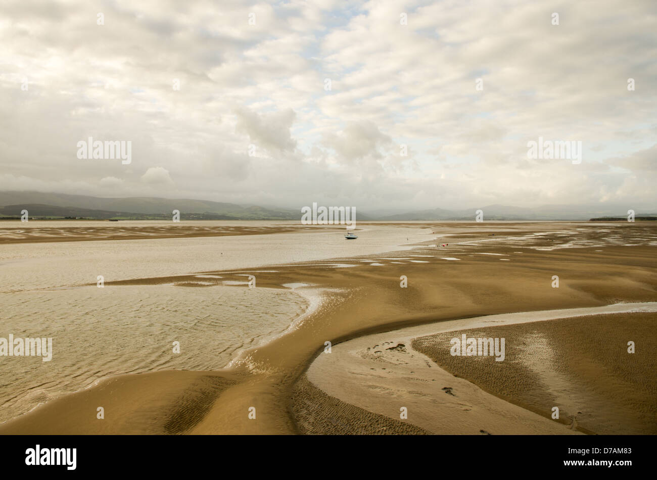 A shallow bay during low tide with sand formations and distant hills covered in low grey clouds. Duddon channel mudflat. Stock Photo