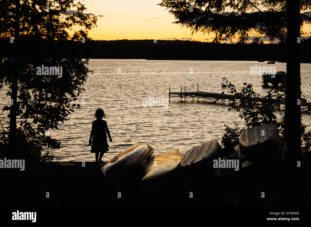 A Young Girl Watches A Sunset Next To Some Boats On The Shore Of Beech Hill Pond On A Summer Evening;Otis Maine USA Stock Photo