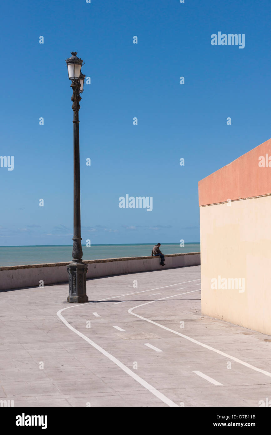 Solitary man sitting on seafront wall Cadiz Andalusia Spain Stock Photo