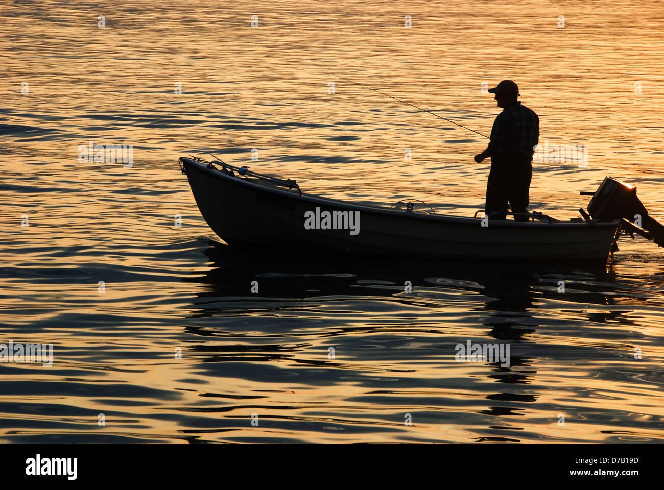 Silhouette of a man fishing from a boat at sunset Stock Photo