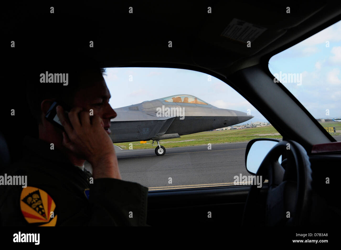 A US Air Force F-22 Raptor stealth fighter aircraft takes off as a security team member watches from his car along the runway April 6, 2013 at Joint Base Pearl Harbor-Hickam, Hawaii. Stock Photo