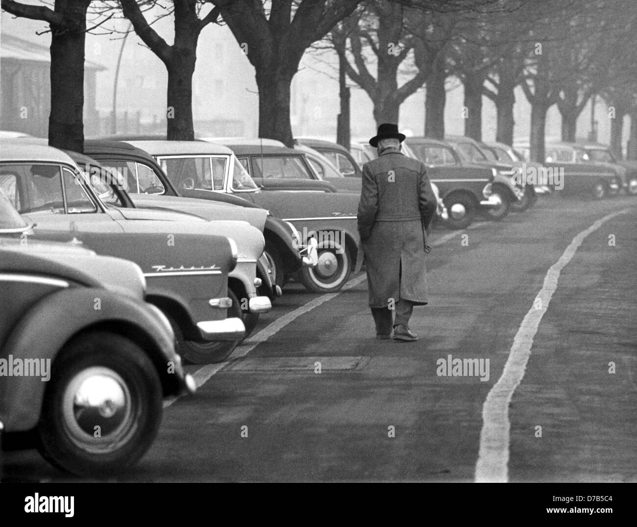 A pedestrian walks past a row of parked cars, photographed on the 20th of March in 1961 in a German city. Stock Photo