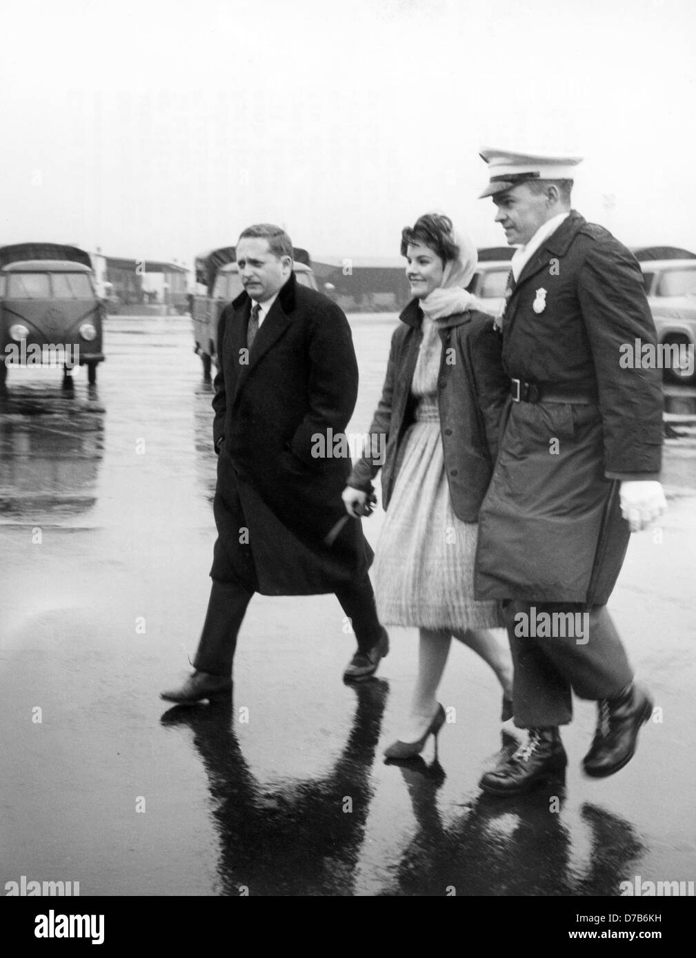 The 16-year-old Priscilla Beaulieu is accompanied by a policeman on the military airbase in Frankfurt on 02 March 1960. The girlfriend and later wife of the American Rock'n Roll singer Elvis Presley had crossed the cordon of police to take leave of Elvis before his flight back to the States. Presley was deployed as a soldier in Hesse and got to know the stepdaughter of a Canadian air force officer in Bad Nauheim in 1959. They married in Las Vegas in 1967. Stock Photo
