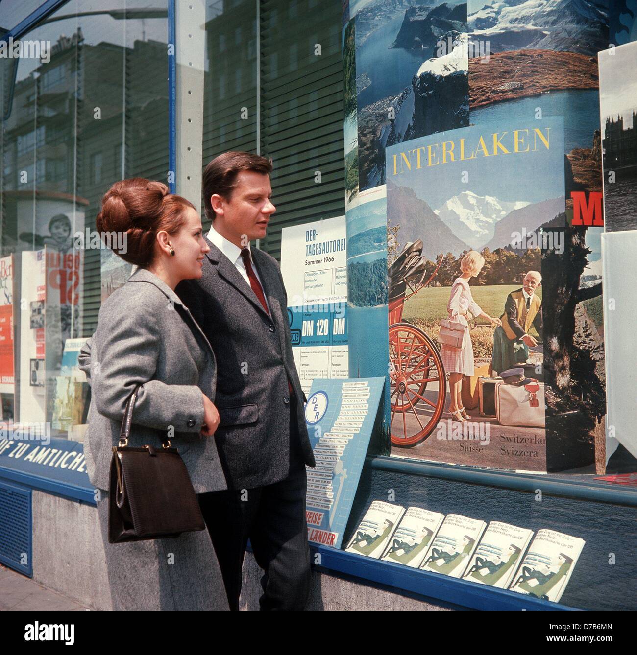 A young couple has a look at a poster advertising for the Swiss town Interlaken in the window shop of a travel agency (picture from the 1960s). Stock Photo