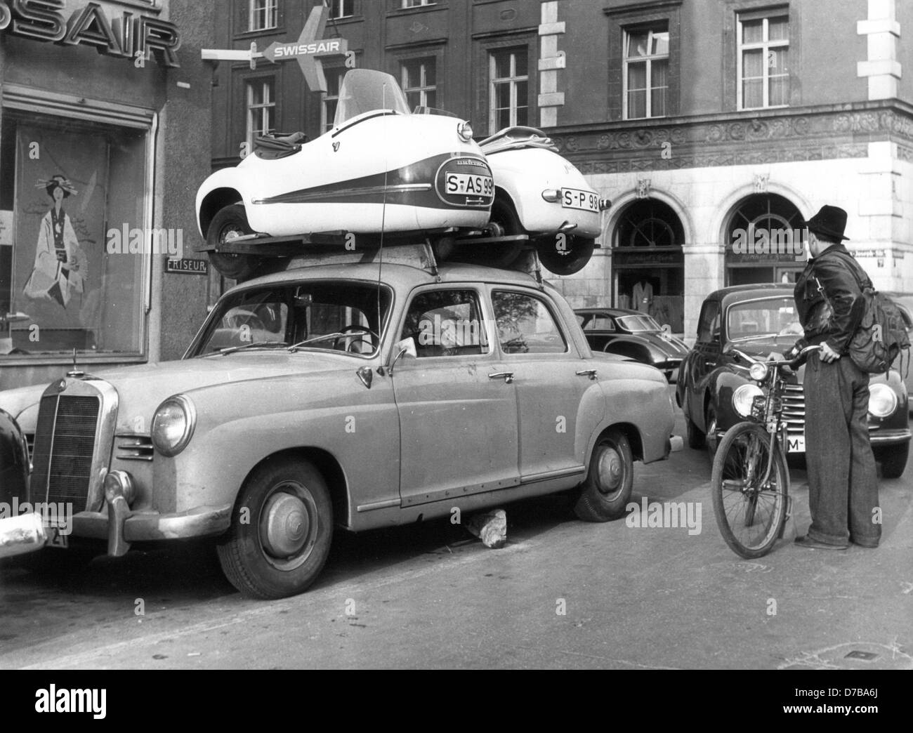 A cyclist watches a parked car, on which two small single-seaters are fixed onto the roof in October 1957 in Munich. Stock Photo