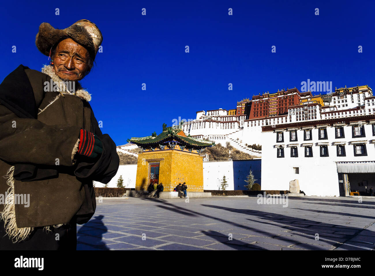 Old Tibetan man with fur hat standing in front of Potala palace in Lhasa, Tibet, China Stock Photo