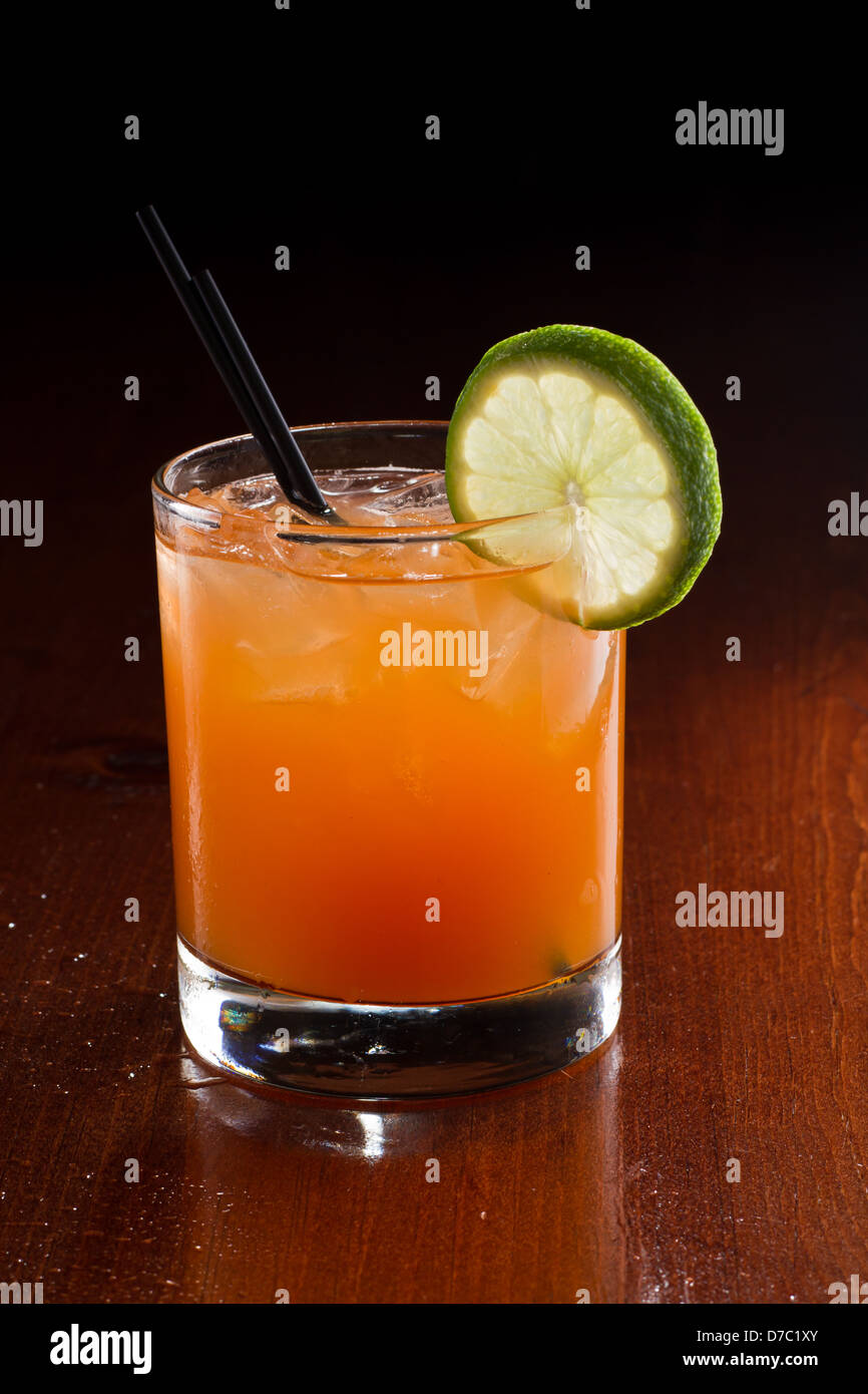 tropical juice cocktail served on a dark bar setting garnished with a lime wheel Stock Photo