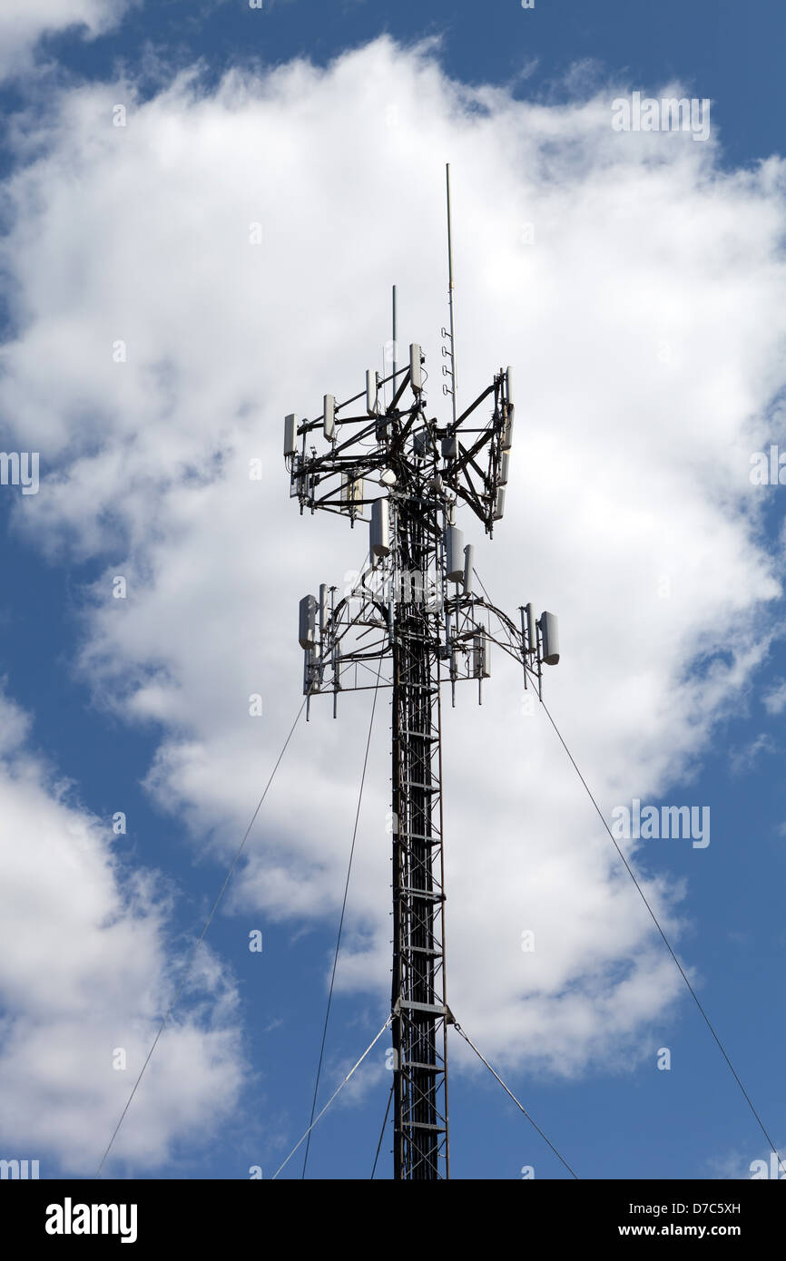 A cellular antenna tower isolated over a blue sky with white fluffy clouds. Stock Photo