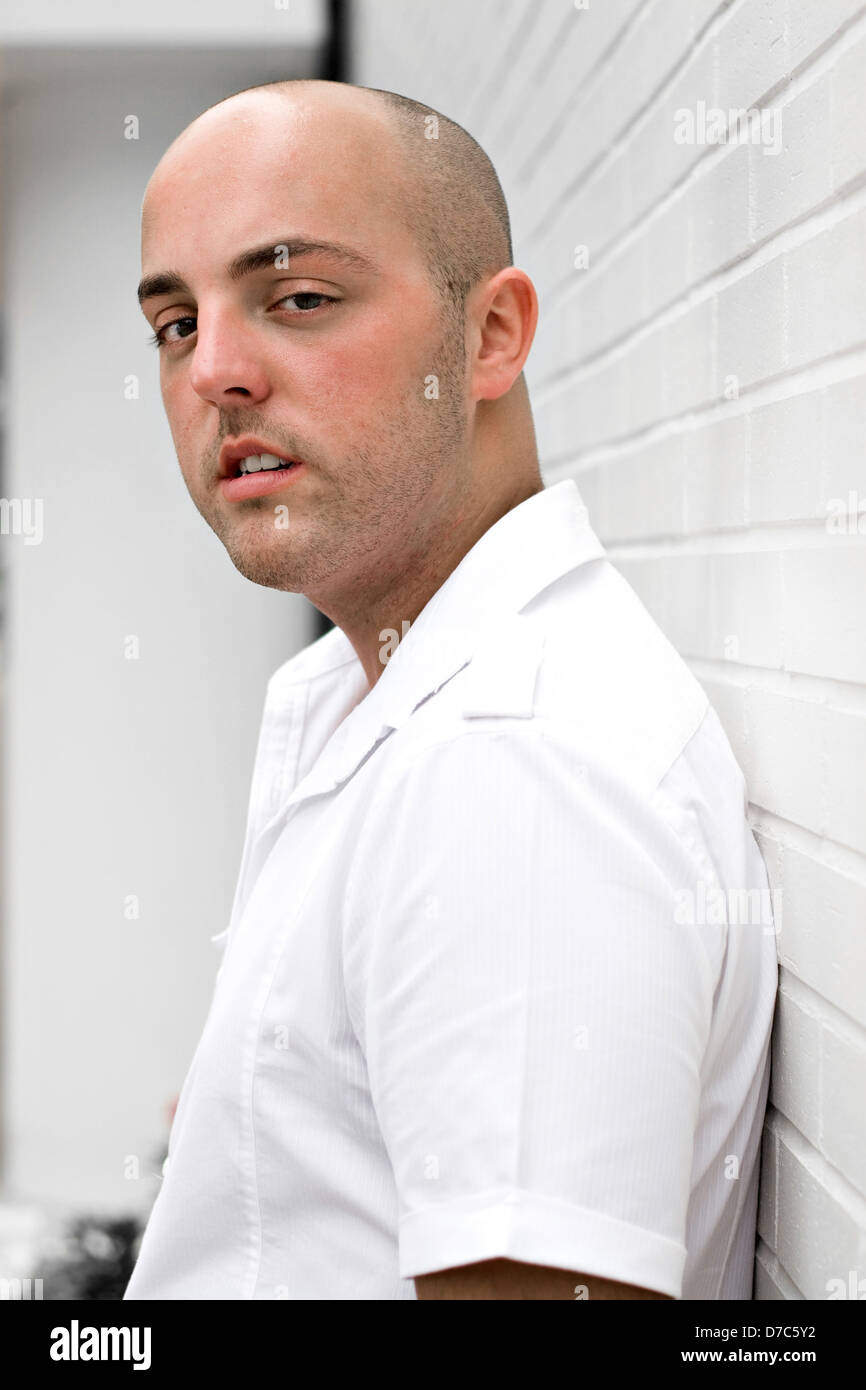 Portrait of a serious young man in the city leaning against a white ...