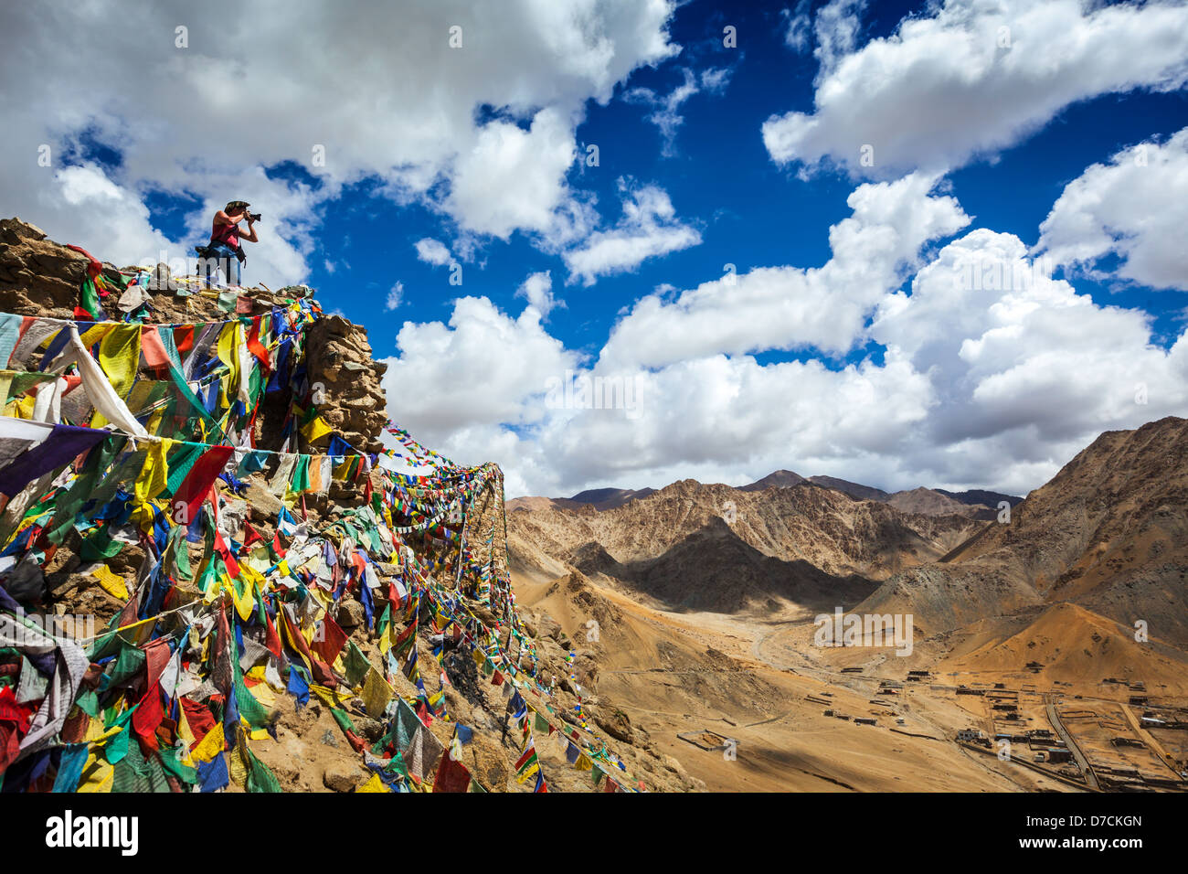 Travel photographer taking photos in Himalayas mountains on cliff with Buddhist prayer flags. Leh, Ladakh, Jammu and Kashmir Stock Photo