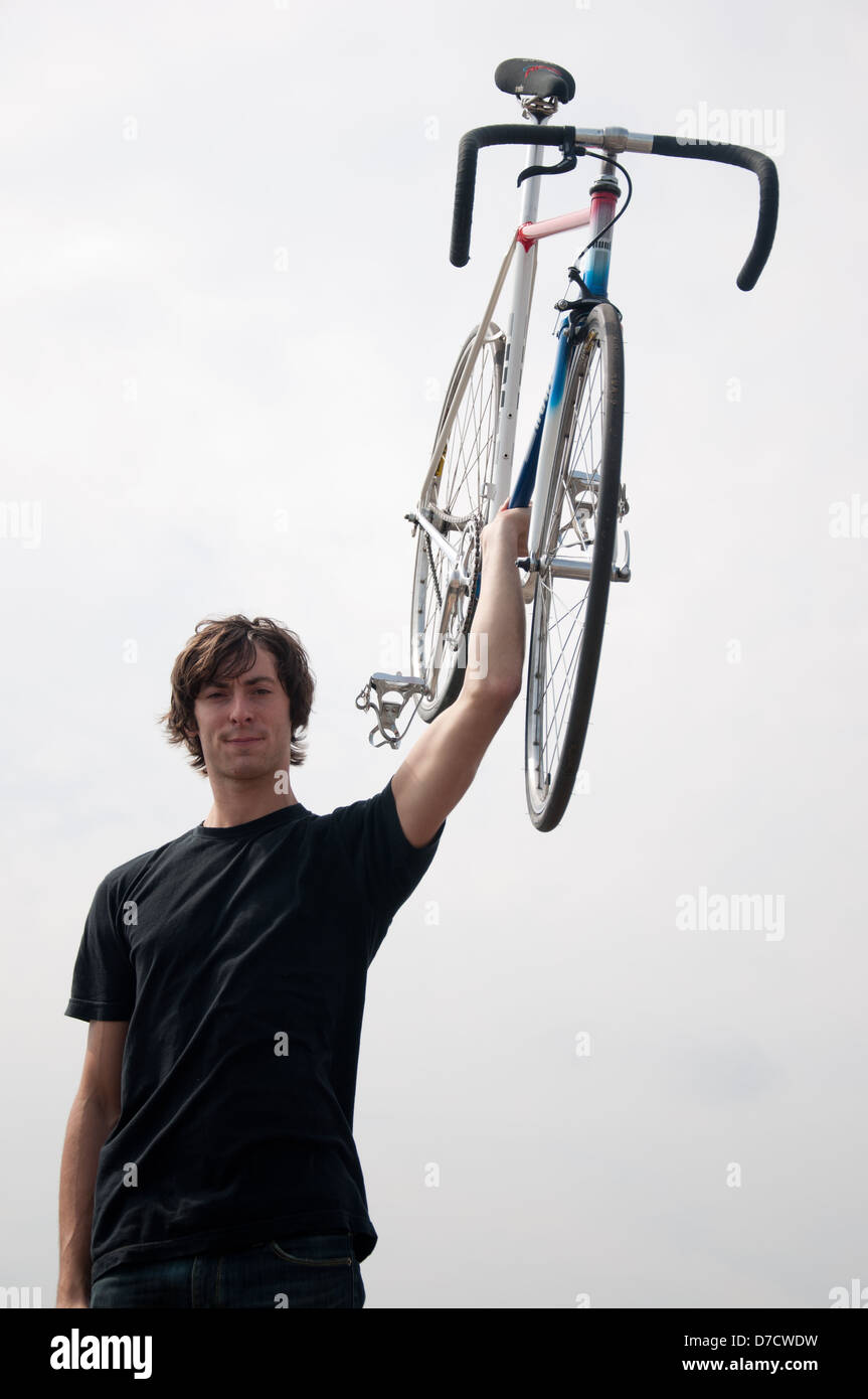 A man holds his lightweight fixed gear road bike above his head. Stock Photo