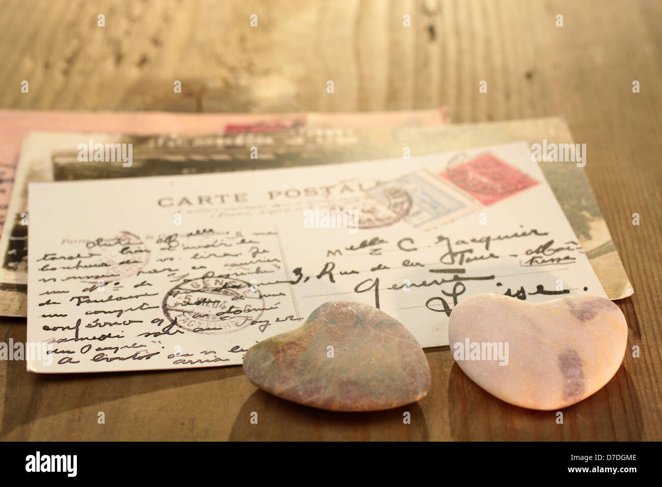 Two dark stone hearts with old French postcard on wooden desk Stock Photo