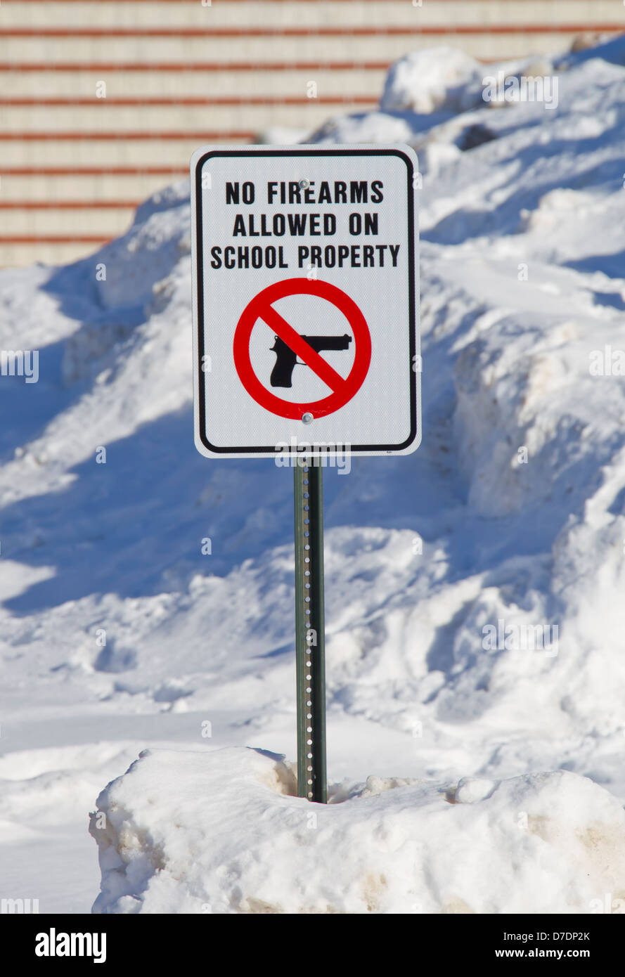 Full View of No Firearms Allowed on School Property Sign outside a school in the snow. Stock Photo