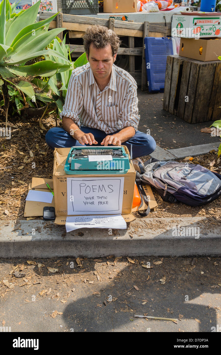 A 25-30 year old male sits on the ground with his Smith-Corona typewriter on a cardboard box selling original poems. Stock Photo