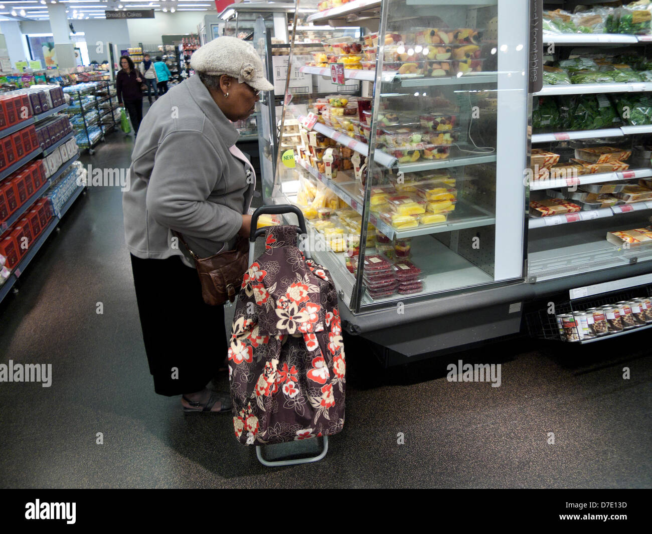 Elderly black woman shopper shopping for food looking at fruit display with a shopping bag trolley Marks & Spencer store Cardiff Wales UK KATHY DEWITT Stock Photo