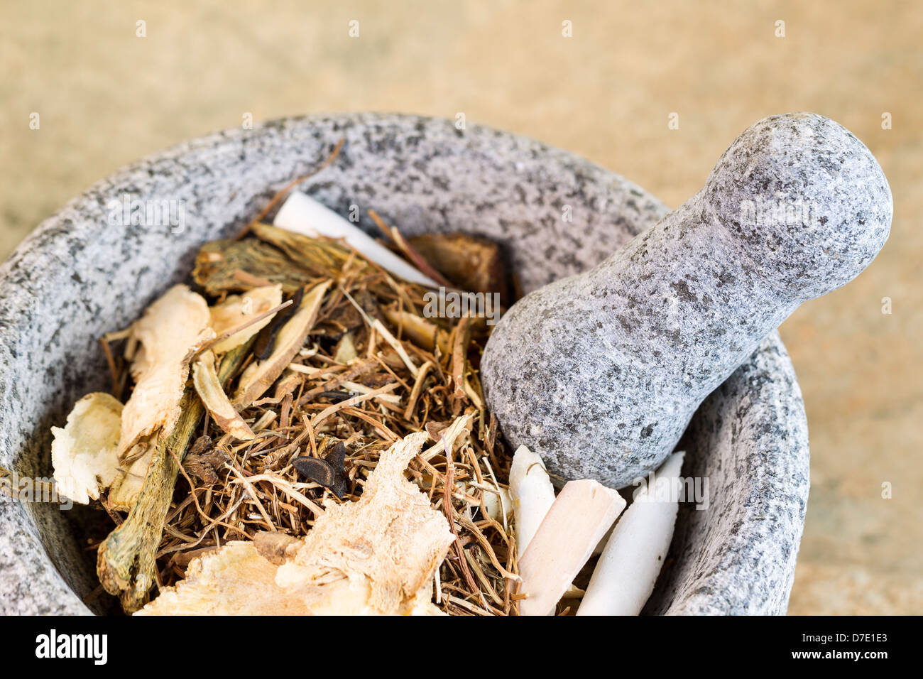 Closeup horizontal photo of a natural stone pestle in stone bowl filled with Chinese herbs used for medicine Stock Photo
