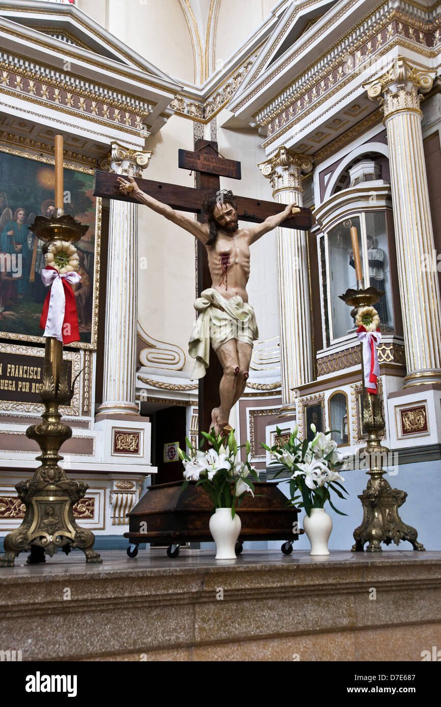 polychrome statue of crucifixion martyred Christ on wooden cross with Easter flowers & rosettes Church of the Company of Jesus Stock Photo