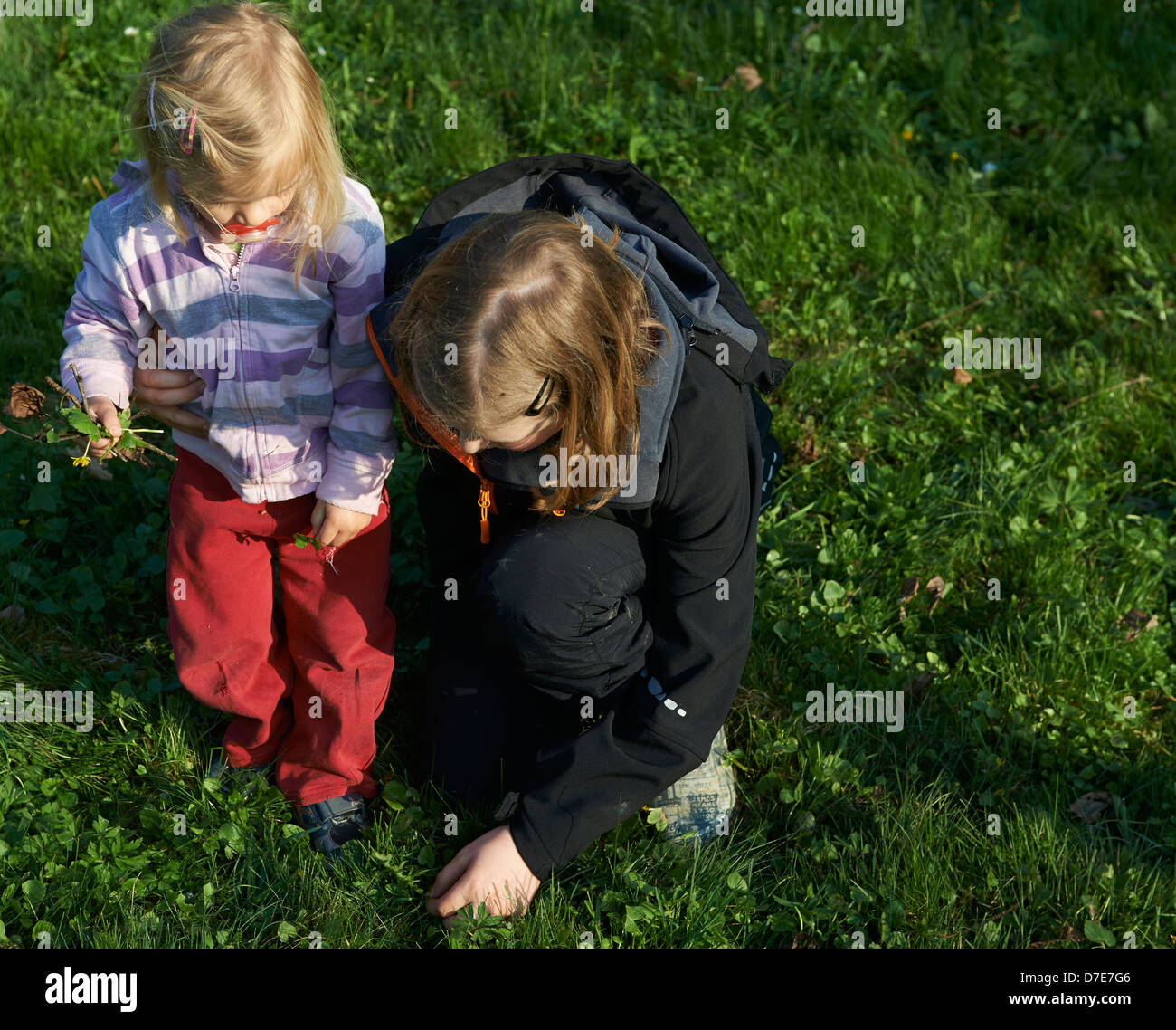 Two children blond girls playing with grass garden and flowers summer time Stock Photo