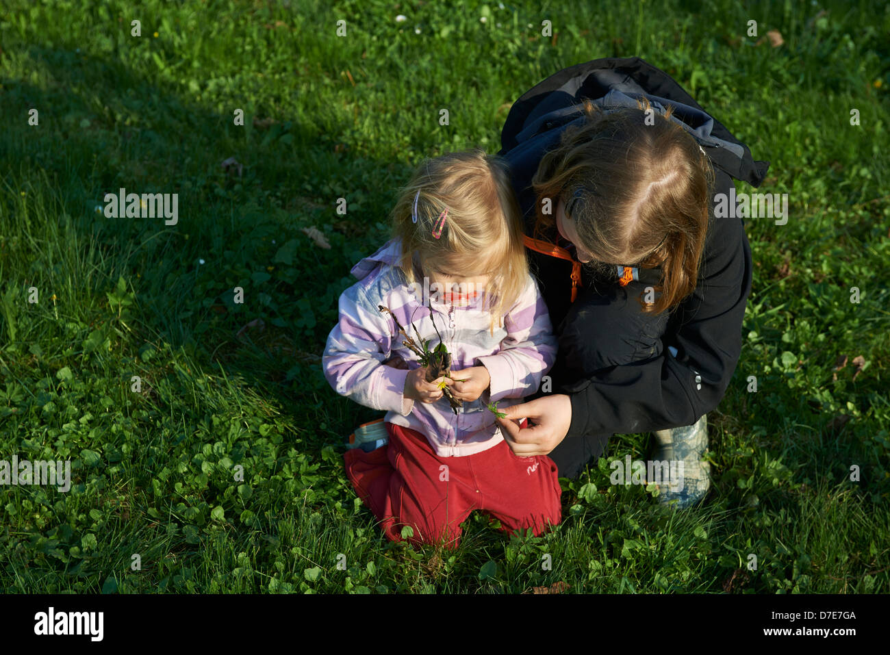 Two children blond girls playing with grass garden and flowers summer time Stock Photo