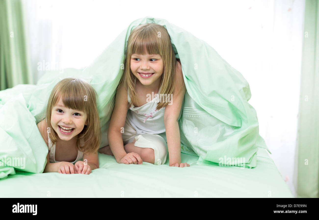 Two little girls lying under blanket on bed Stock Photo