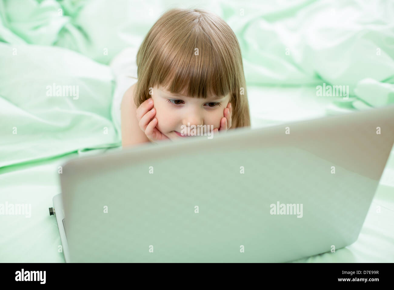 concentrated serious kid girl lying on bed with notebook Stock Photo