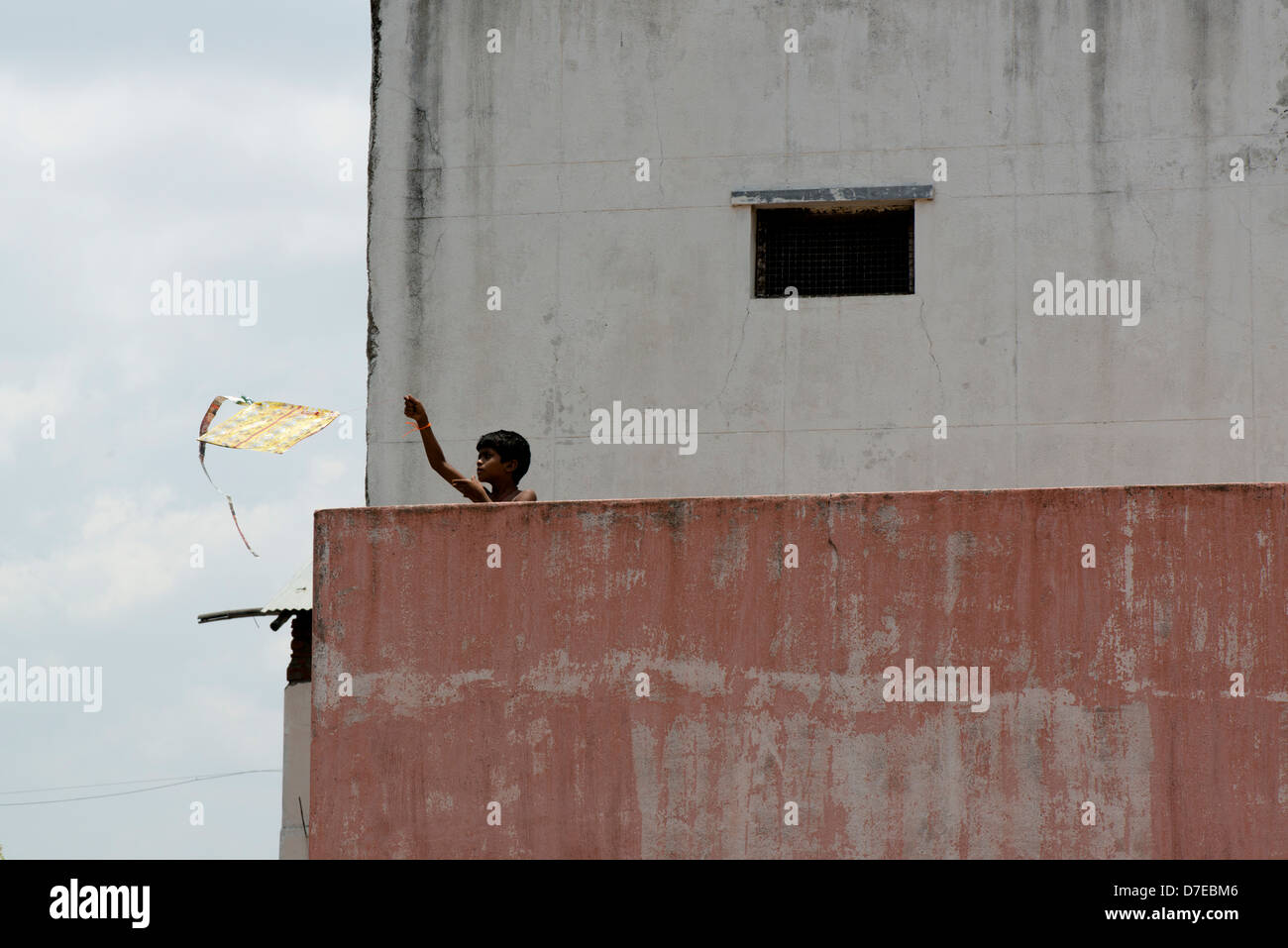 A boy launches his kite from a rooftop in Tiruvannamalai, Tamil Nadu, India Stock Photo