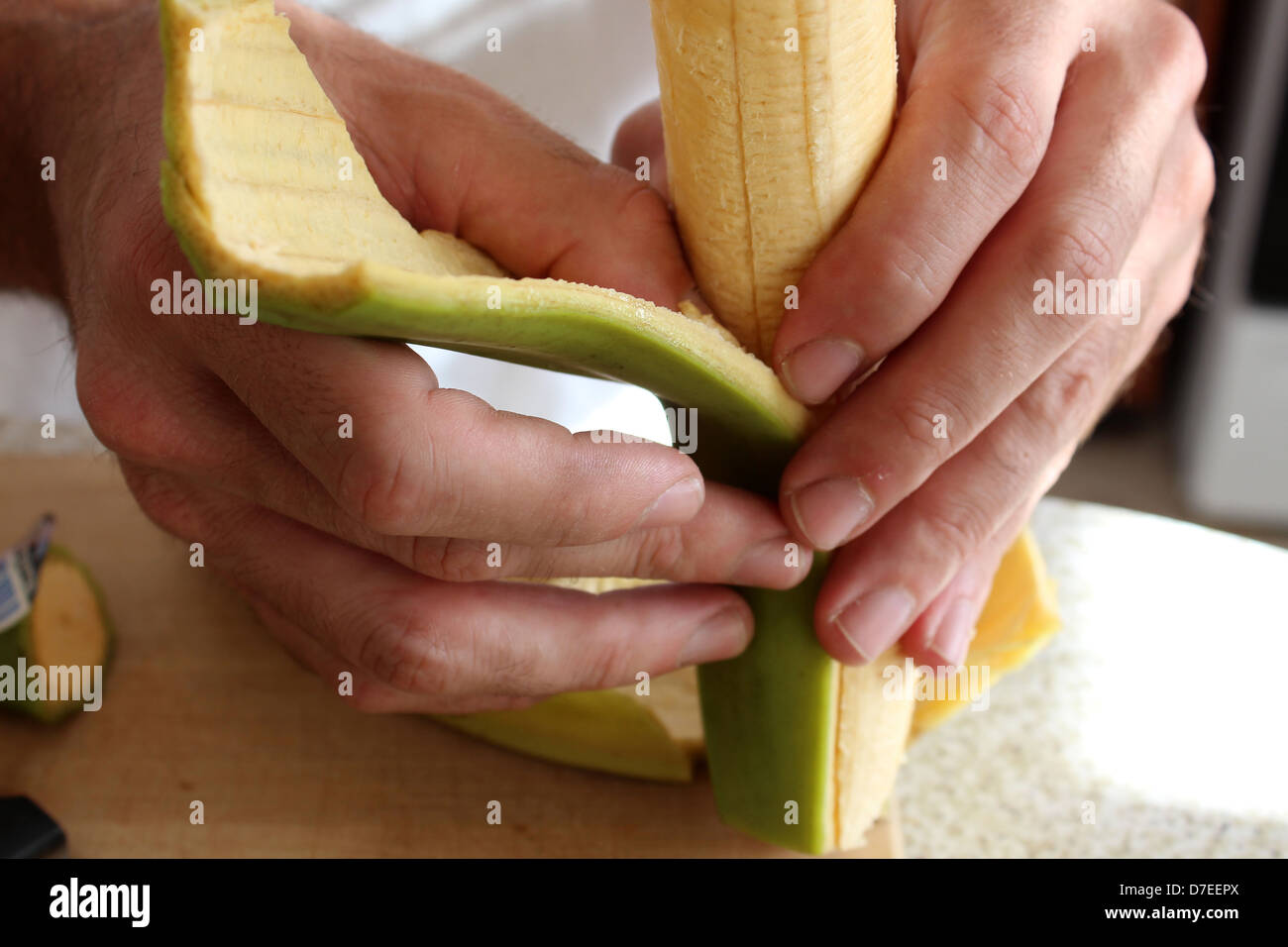 Man's hands carefully peeling back the thick skin of plantain fruit to ready for frying in virgin oil and light seasonings. Stock Photo