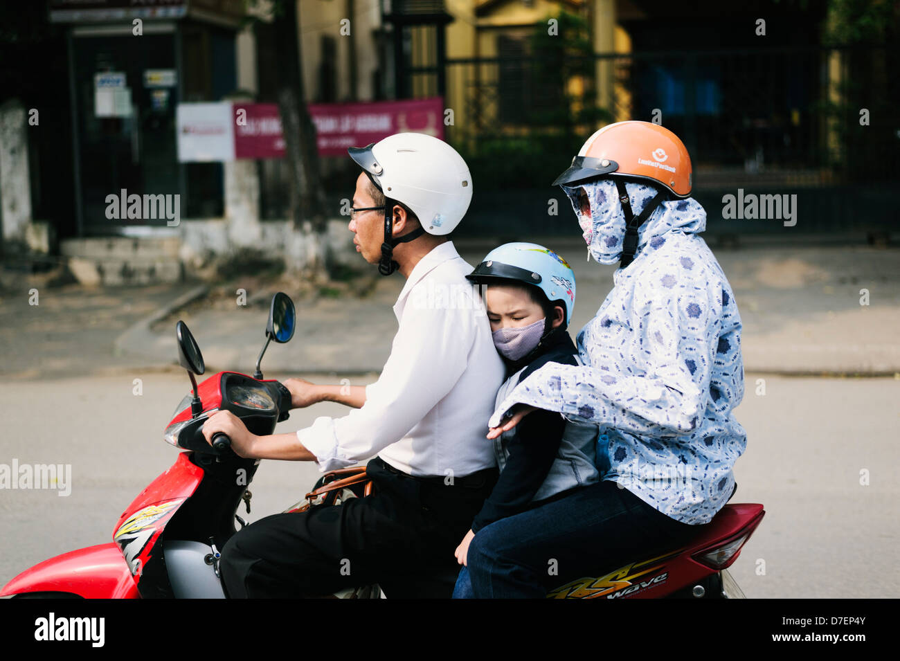 Hanoi, Vietnam - 2 adults and a small child riding a motor scooter with face masks Stock Photo