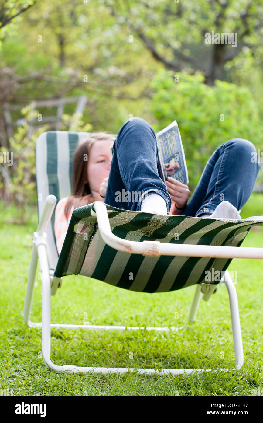 Teenage girl lying on a sun lounger and read a book outside in the garden. Stock Photo