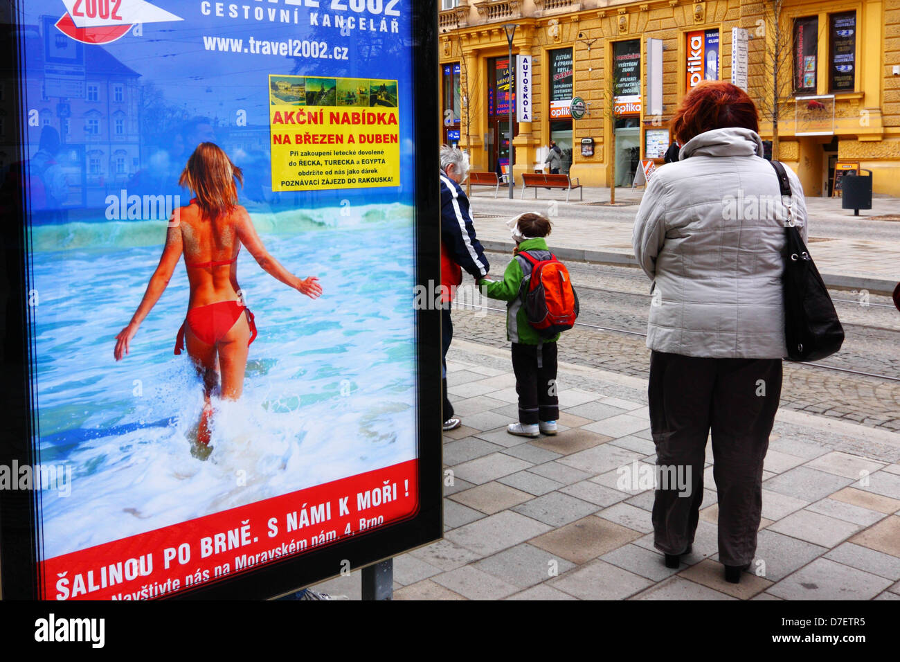 People in winter clothes waiting by tram stop with big poster with bikini model advertising beach vacations. Brno, Czech Repu Stock Photo