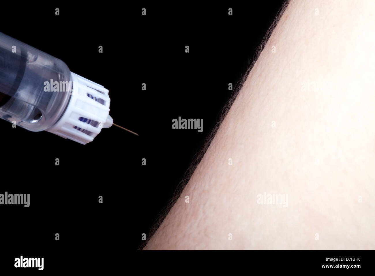 A macro shot syringe full insulin about to penetrate arm young adult man Diabetes. Isolated on black background. Stock Photo