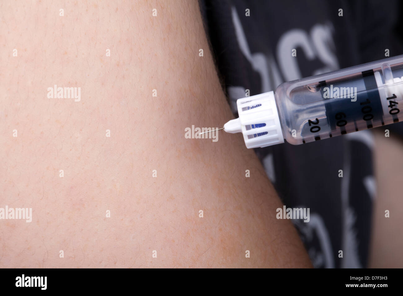 A macro shot of a syringe full of insulin about to penetrate the arm of a young adult man with Diabetes. Stock Photo