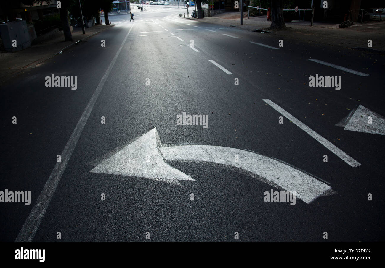 Directional arrow pointing left on an empty street in Tel-Aviv Israel. Defocused in background man is crossing street. Shot at Stock Photo