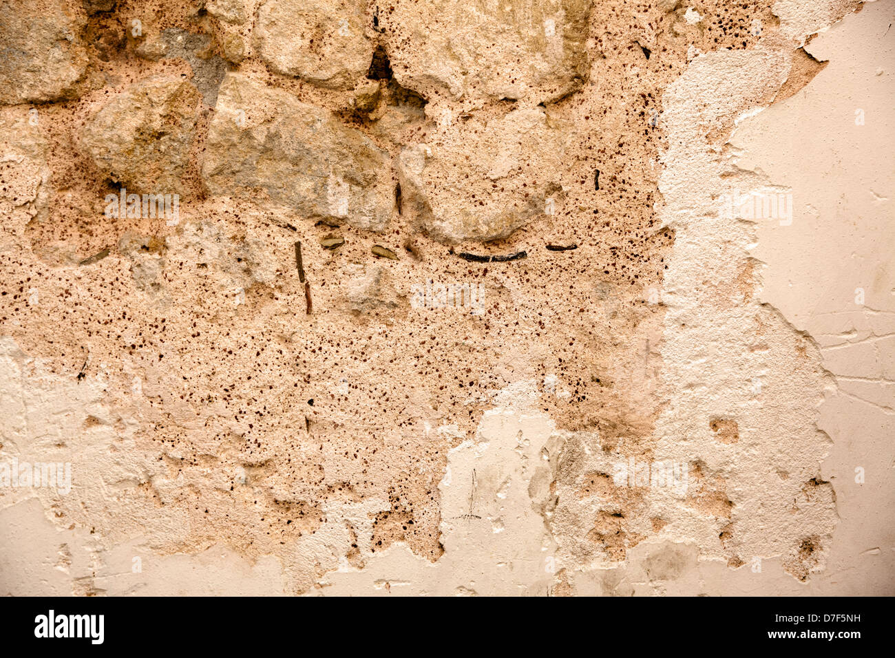 Close up of a very old wall, most of the white plaster and paint peeled off it, revealing the stones beneath. Stock Photo