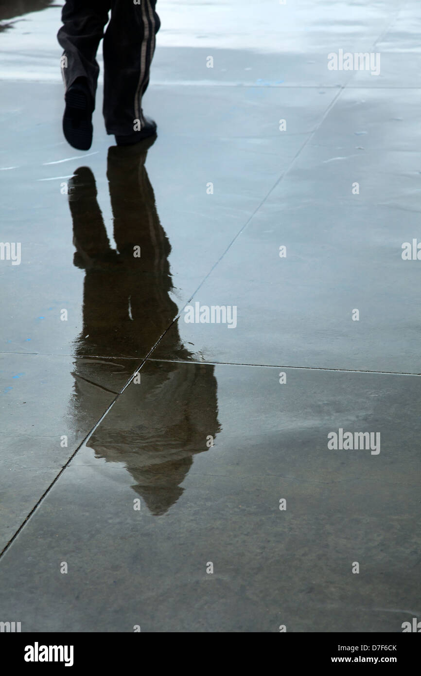 A pedestrian's reflection on the wet concrete pavement on an inclement and wet winter day. Stock Photo