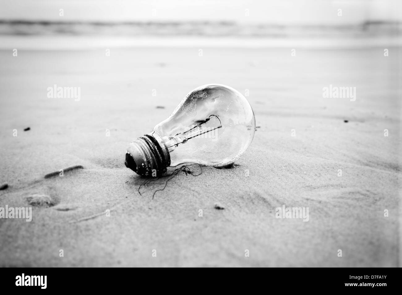 A used burnt-out incandescent light bulb abandoned on sandy beach in inclement weather. Relates to energy conservation Stock Photo
