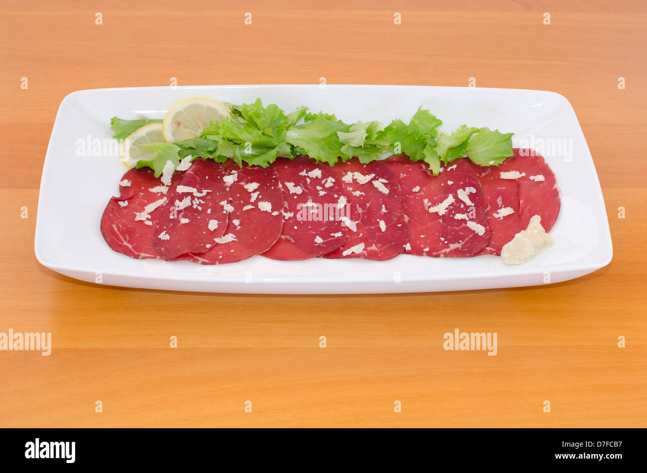 Bresaola with rocket cheese, green salad and lemon on wooden table Stock Photo