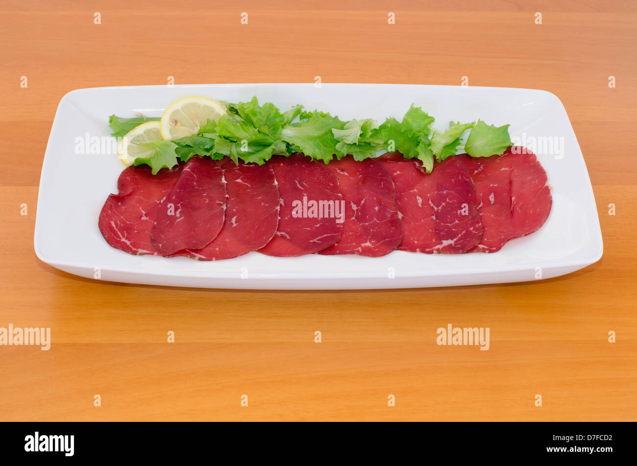 Bresaola with lemon and green salad on wooden table Stock Photo